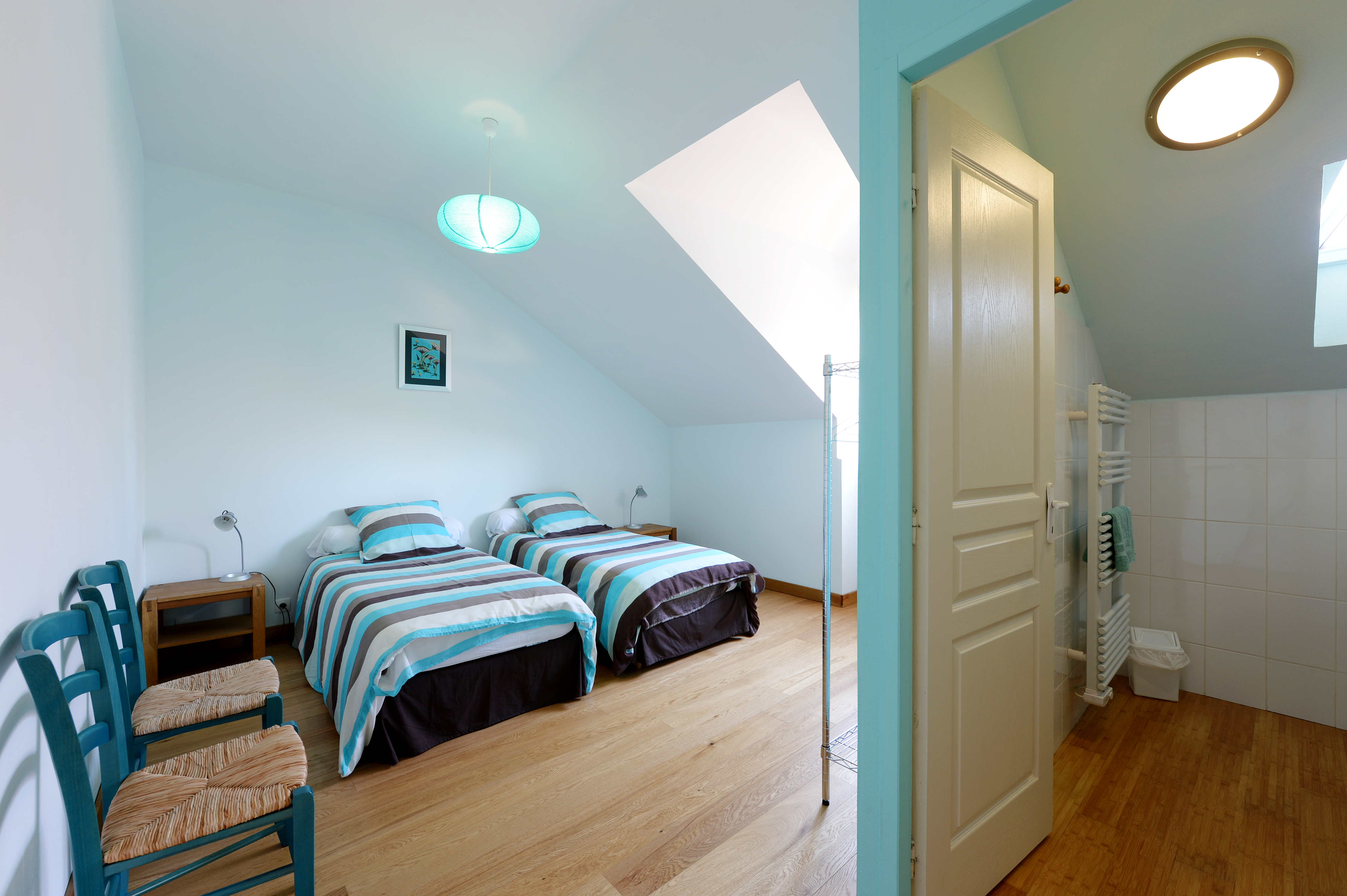 Chambre bleue lumineuse avec trois lits simples et salle de bain privée, alliant confort et simplicité