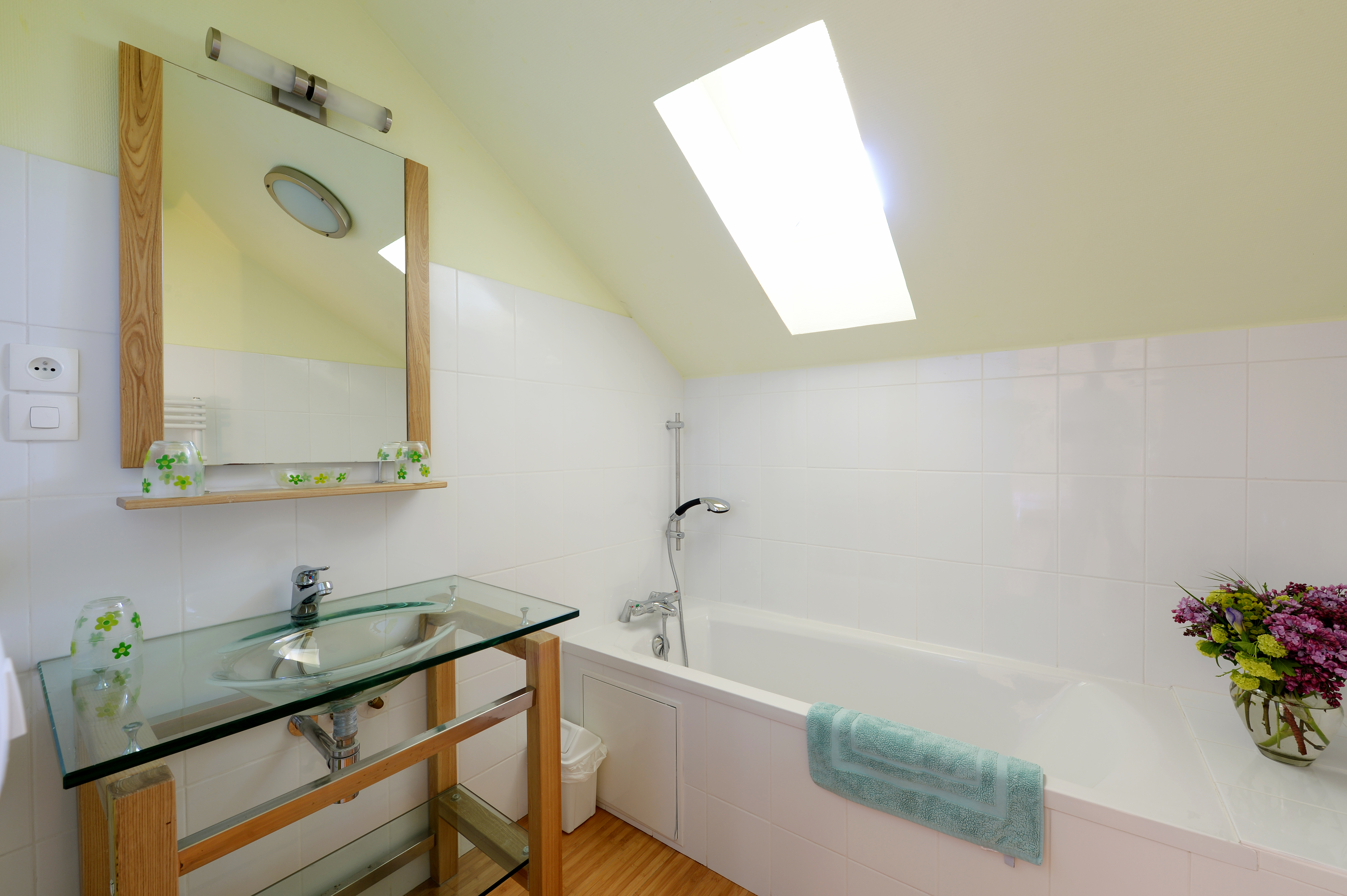 Salle de bain lumineuse avec baignoire sous un velux, offrant une ambiance fraîche et propre.